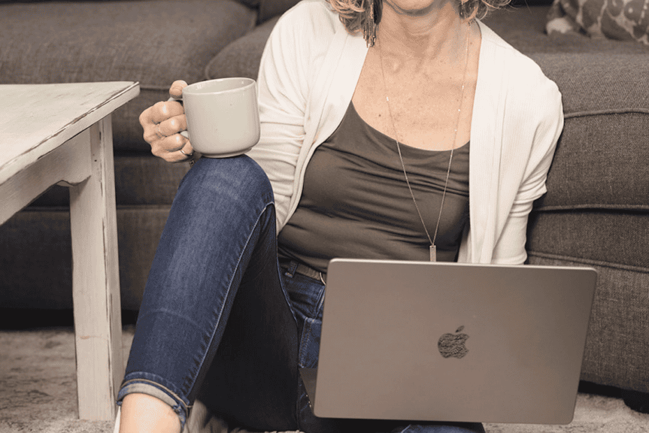 A lady on her laptop holding a cup of coffee learning how to set work boundaries.